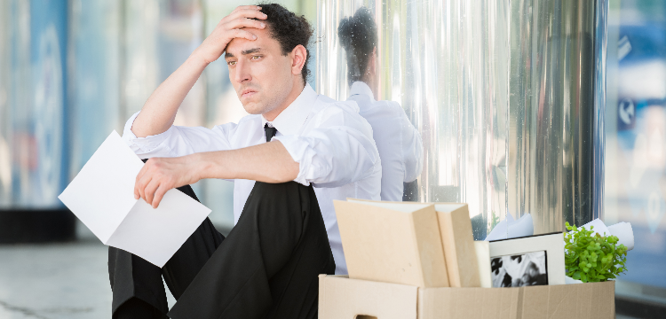 Recently laid off office worker sitting outside with hand on forehead, looking stressed
