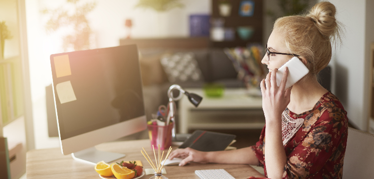 Young woman on phone in home office while working on computer